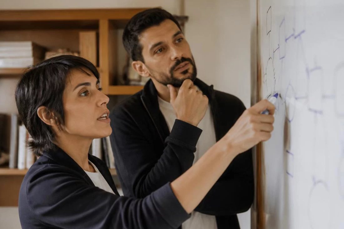 Dois alunos em pé diante do quadro branco, riscando a ordem em que o argumento será apresentado